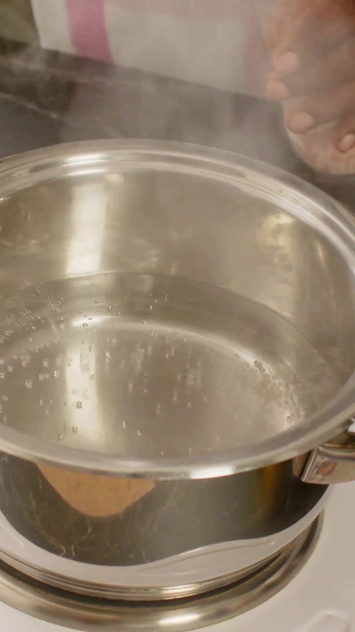 Vertical video: Reaching for pink crystals to season, cook shifting pan off hotplate on counter