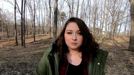 A-pretty-teenage-female-wearing-a-green-coat-strolls-through-the-park-with-a-serious-look-on-her-face