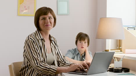 working mom using laptop next to her focused daughter