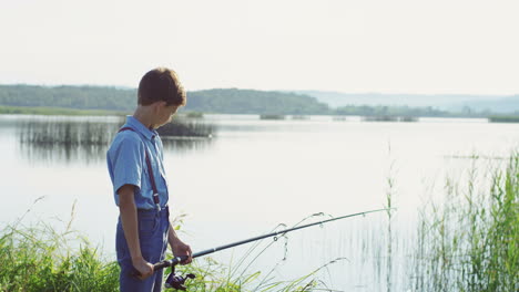 夏の日の朝、絵のように美しい湖岸で大きな棒で釣りをする十代の少年