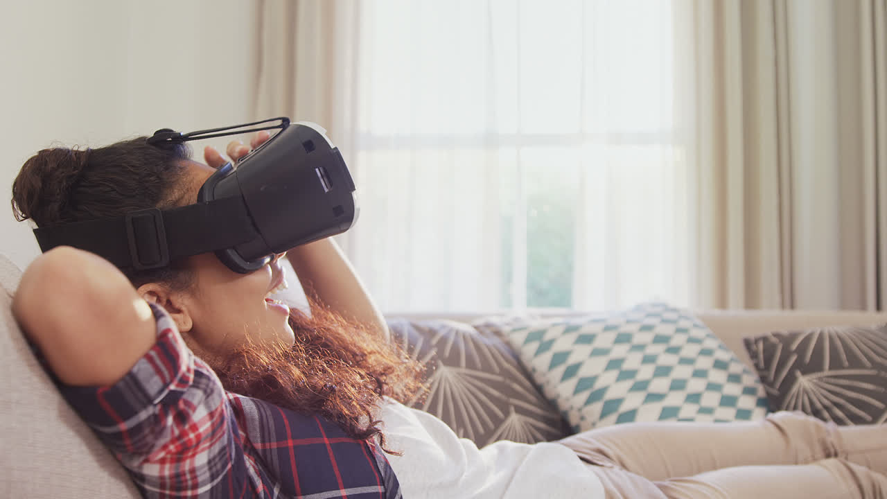 mujer sonriente acostada en el sofá usando auriculares de realidad virtual en casa 4k 4k