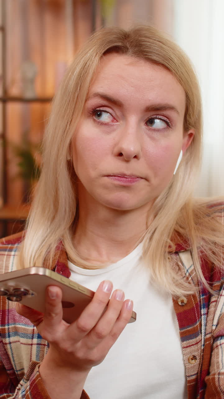 Adult woman listening to voice message with wireless earphones at home surprised by unexpected audio