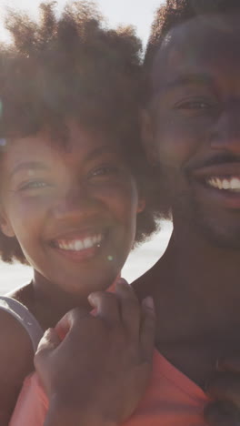 portrait of smiling african american couple embracing on sunny beach