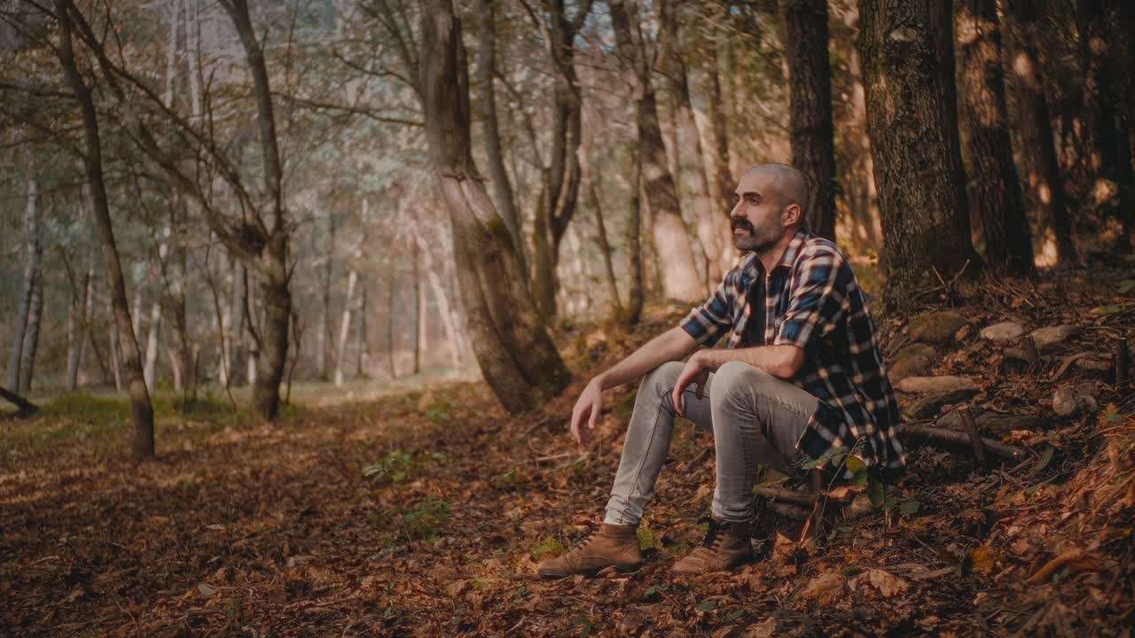 Man on stair in forest enjoys autumn scenery. He looks thoughtful and serene. Cozy and peaceful nature footage