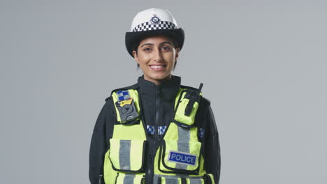 studio portrait of smiling young female police officer against plain background