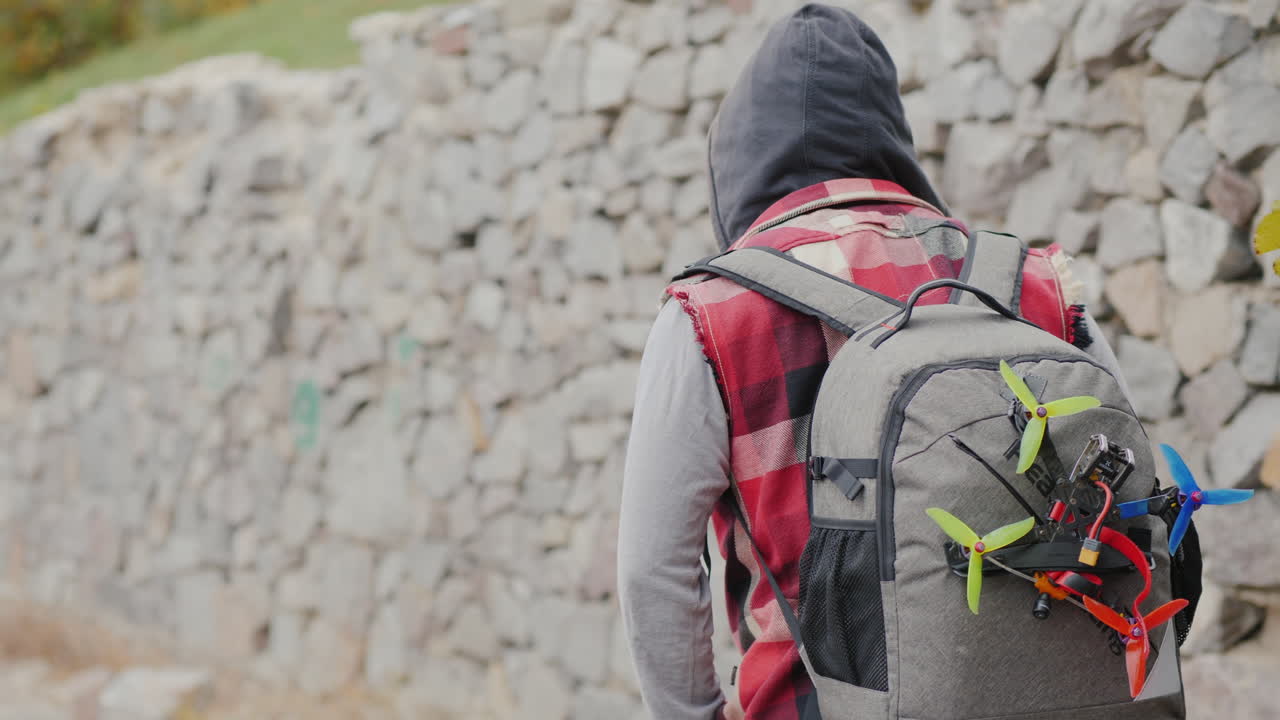 un hombre con una mochila detrás de él y un dron deportivo camina a lo largo de una pared de piedra