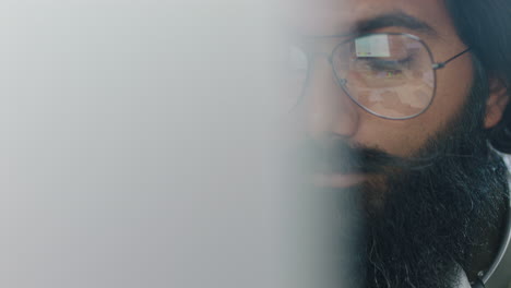 close-up-portrait-young-indian-businessman-using-computer-brainstorming-browsing-online-research-ideas-for-startup-company-project-networking-reading-email-wearing-glasses-in-office