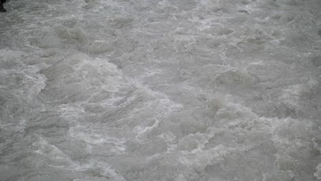 fast streaming gray melted water in a small river and sloshing on the rocks and stones in lauterbrunnen switserland. close-up slow-motion shot