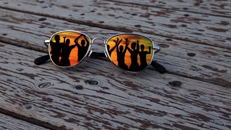 sunglasses reflecting silhouettes of friends enjoying a vibrant sunset rest on a weathered wooden table, capturing the essence of summer memories and shared experiences