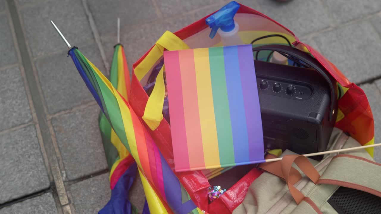 múltiples banderas lgbtq del arco iris y sombrillas tendidas en el suelo en un fondo urbano con casas en el fondo borroso
