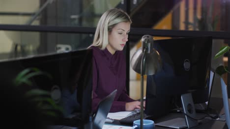 video of caucasian businesswoman sitting at desk working at computer at night in office