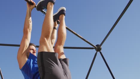 hombre caucásico en forma haciendo ejercicio afuera, haciendo levantamientos de piernas en un marco de escalada