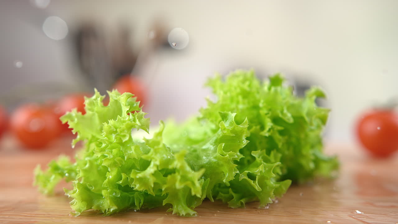 Green Curly Lettuce Falling Onto The Wooden Kitchen Table, Bouncing And Splashing Water Droplets Around in Macro and Slow Motion