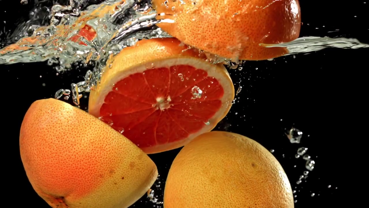 Mezze di pompelmo fresco e frutti interi che schizzano nell'acqua
