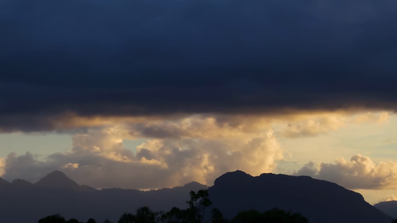 Observe the interplay of dark clouds and mountain silhouettes as evening light fades, creating a serene and dramatic landscape.