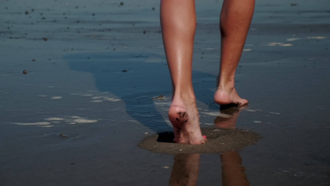 Donna che cammina a piedi nudi sulla sabbia bagnata