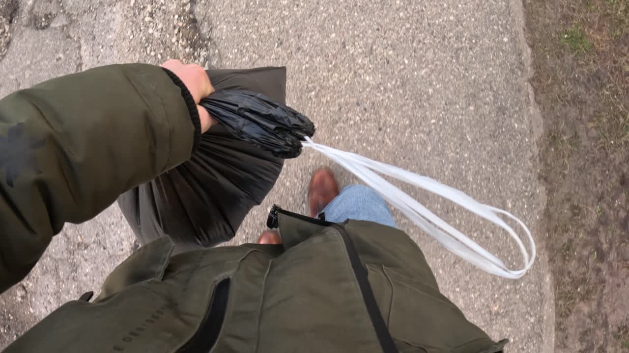 A POV shot looking down while walking and carrying a bag of rubbish outdoors, showing a simple moment of daily responsibility.
