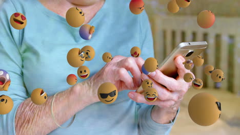 animation of emoticons floating over hands of caucasian senior woman using smartphone