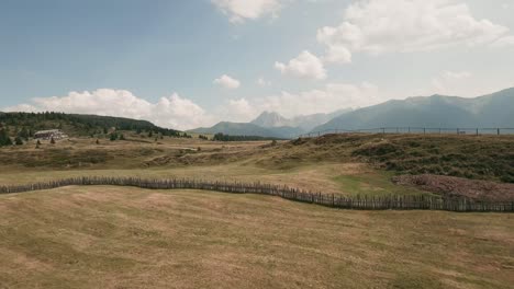 fpv drone glides low over the picturesque italian mountain plateau, skimming close to a wooden cottage and cows in the serene enclosure near the charming village of luzen