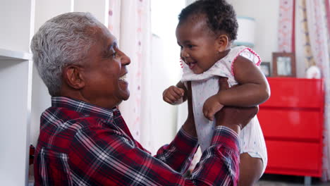 abuelo levantando a la nieta bebé en el aire y sonriendo en casa