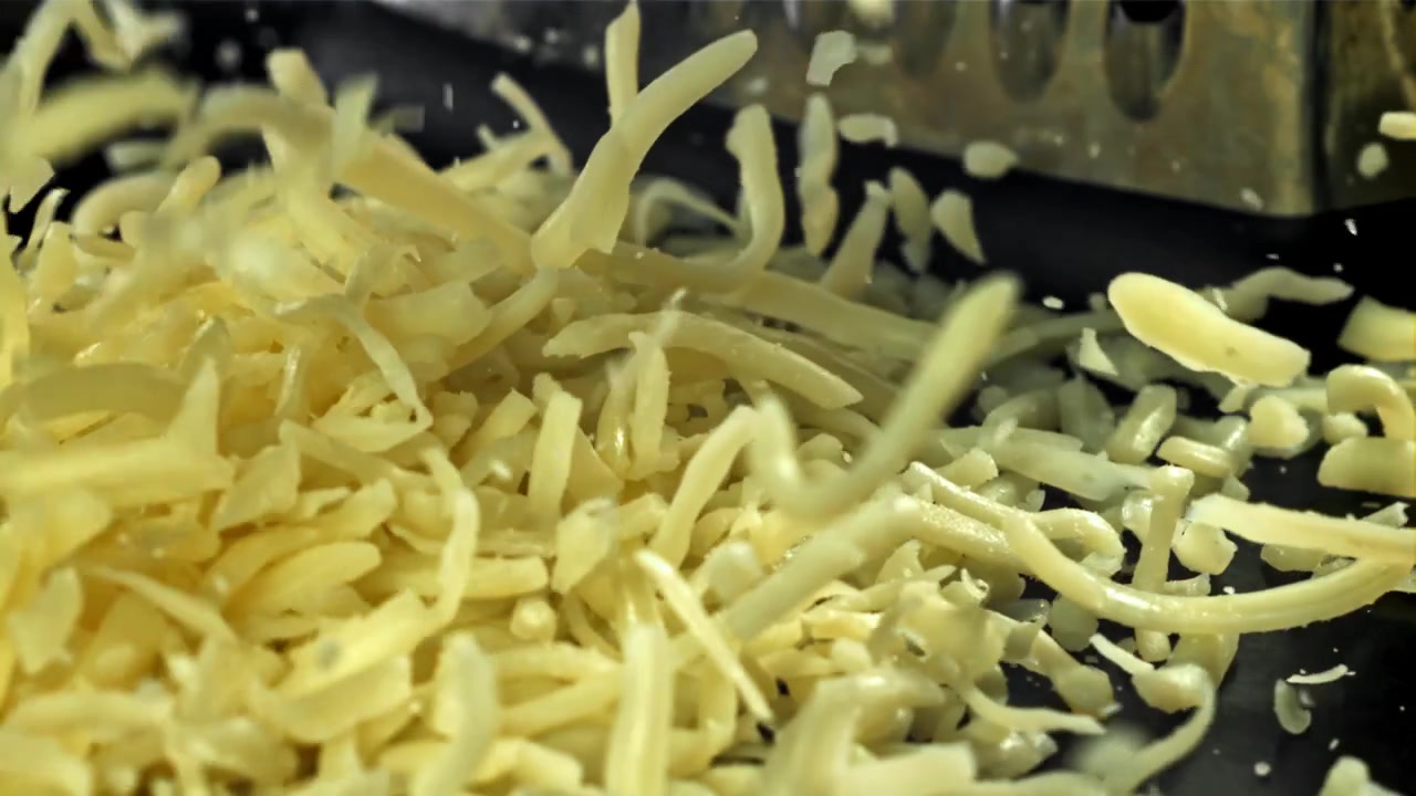 Primo piano al rallentatore di formaggio grattugiato che cade su una superficie nera