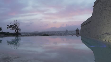 Bewölkter,-Farbenfroher-Blick-Auf-Den-Sonnenuntergang-über-Dem-Großen-Hafen-Von-Valletta-Vom-Luxuriösen-Infinity-Pool-Aus---Zeitlupe