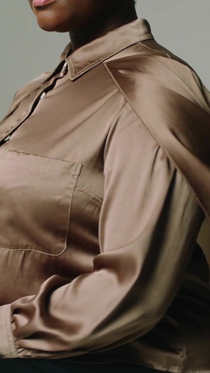 Video verticale: Modella che gira in studio con una blusa di raso color bronzo, la telecamera riprende mostrando le cuciture