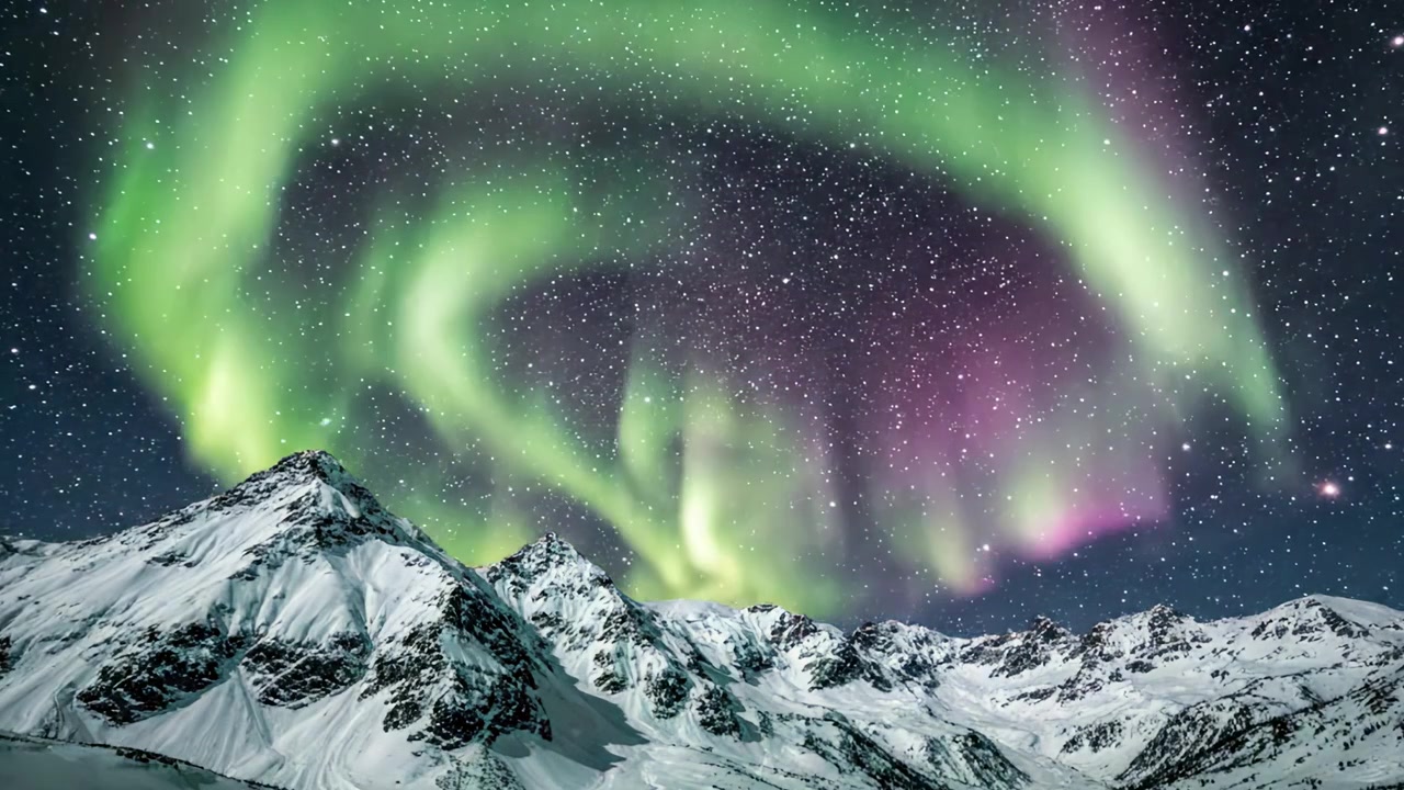 Spettacolare manifestazione di bellezza cosmica: un'affascinante Aurora Boreale illumina montagne innevate sotto un cielo notturno stellato.