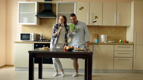 attractive young joyful couple have fun dancing and singing while cooking in the kitchen at home