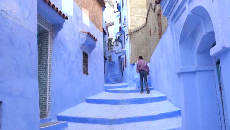 A-man-walking-up-the-blue-stairs-in-Chefchaouen,-the-blue-city-of-Morocco