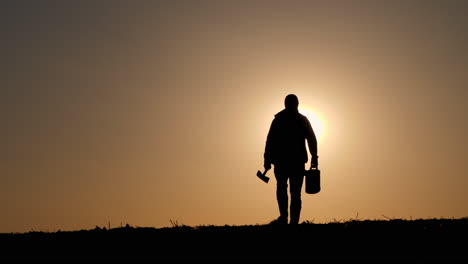 silhouette of a person walking at sunset carrying tools