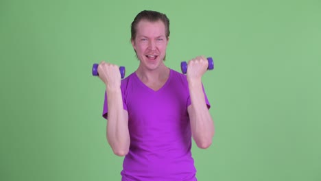 fotografía de estudio de un joven sonriendo y haciendo ejercicio con pesas contra un fondo verde