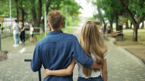 The-guy-and-the-girl-are-walking-in-the-park,-talking.-The-guy-is-holding-a-scooter-in-his-hand.-Happy-walk.-romantic-date