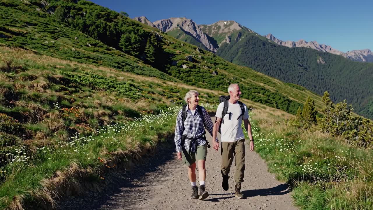 Un video aereo riprende una coppia di anziani che fanno trekking su un sentiero di montagna, circondati da una vegetazione lussureggiante