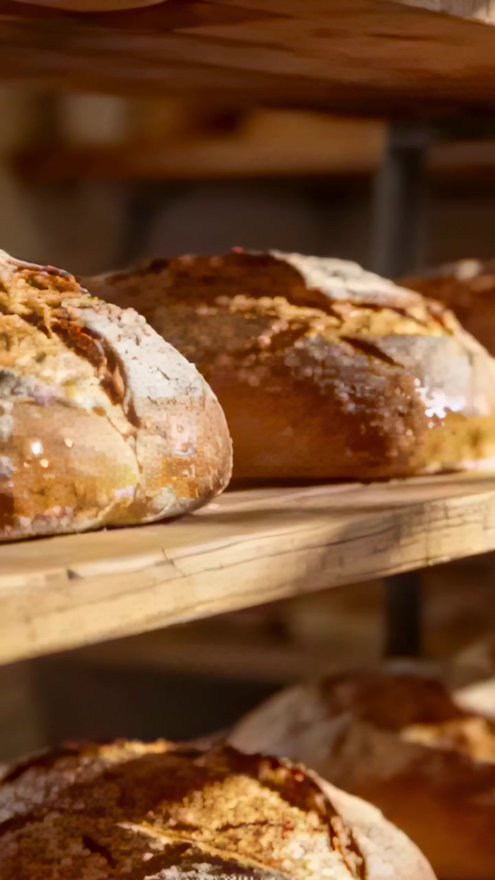 Vertical video: Tracking shot revealing crusty round loaf on middle wooden shelf, flour-dusted