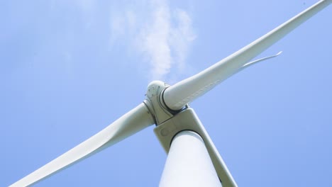 low angle looking up at spinning wind turbine energy generator blades against blue sky