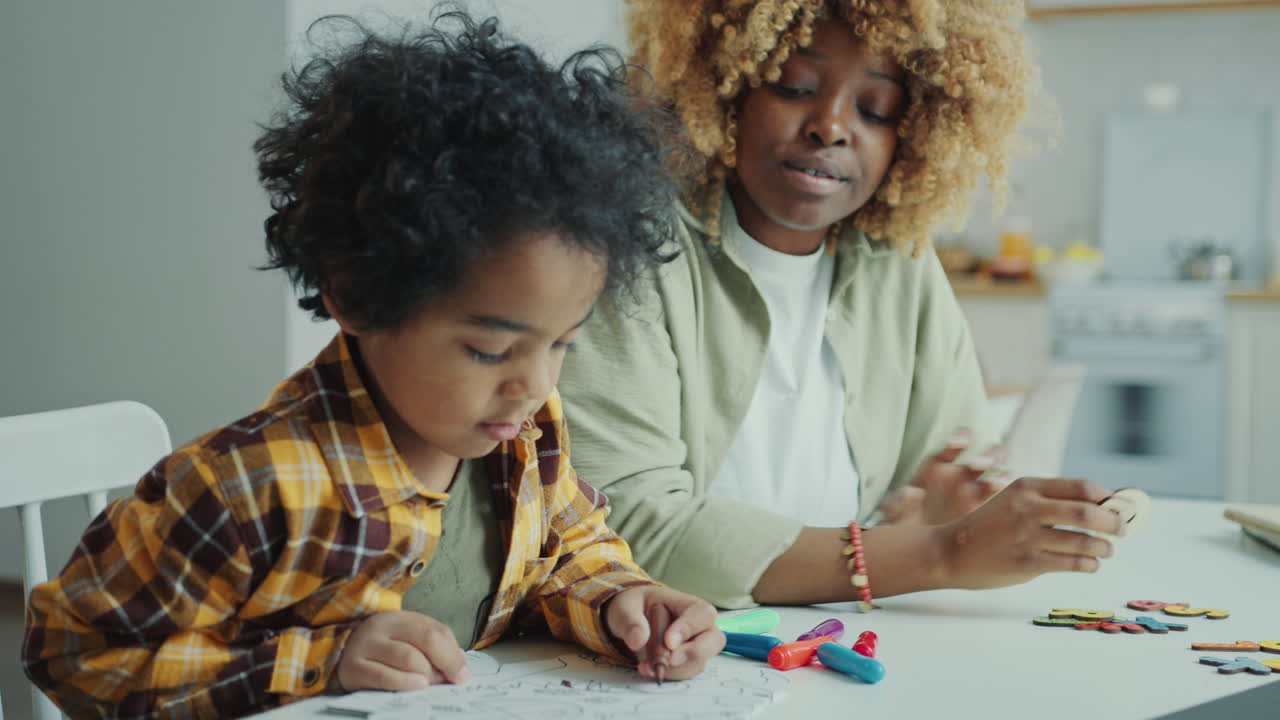 Little African American Boy Drawing on Paper with Mother at Home