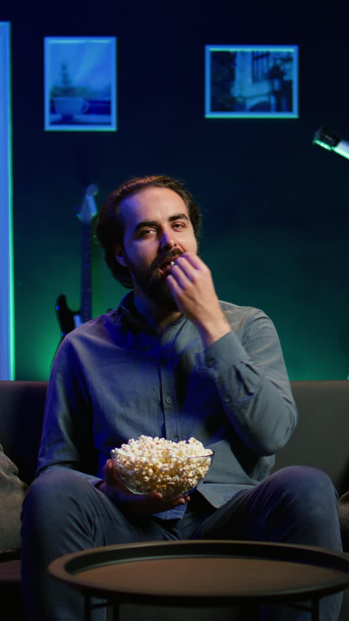 Vertical video Man turning on TV using remote control, eating popcorn