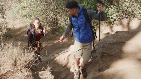 Happy-african-american-couple-hiking-with-trekking-poles-in-forest,-slow-motion