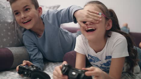 kids playing video games. brother close eyes sister. children have fun together