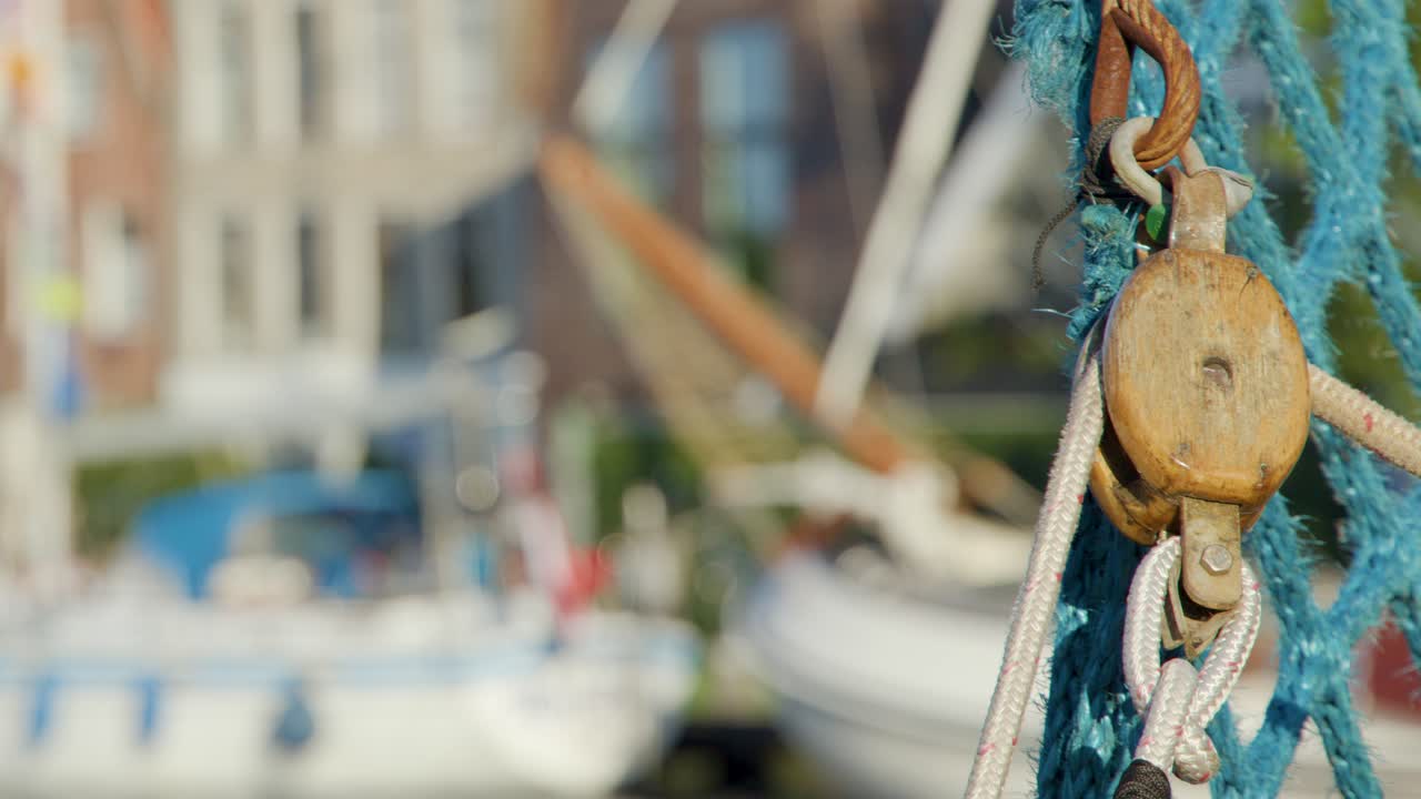 Vista dettagliata di una carrucola usurata e di una rete da pesca su una barca, con canale sfocato, barche ed edifici storici di Haarlem in piena luce diurna.