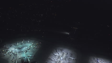 una vista de pájaro de un aeropuerto que muestra varias terminales con aviones estacionados y un avión que se mueve de noche