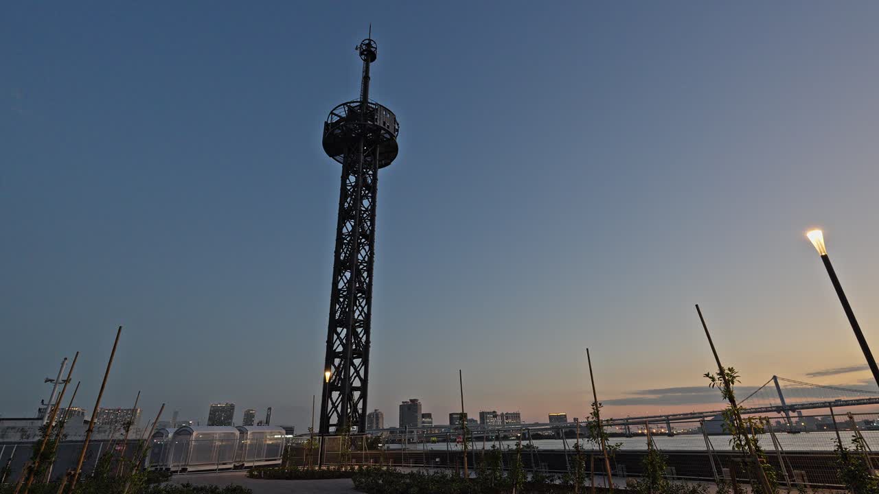 Low-angle shot of the Harumi Signal Station tower with the Tokyo Bay skyline and Rainbow Bridge visible at twilight