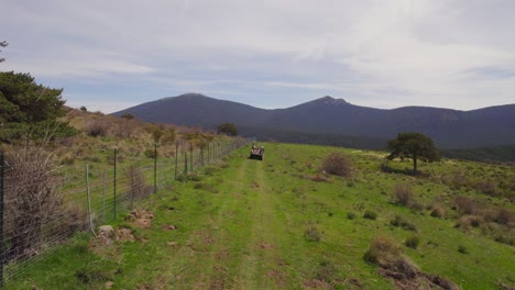 aerial following shot of 4x4 off-road vehicle driving on scenic route between fields and mountains during summer