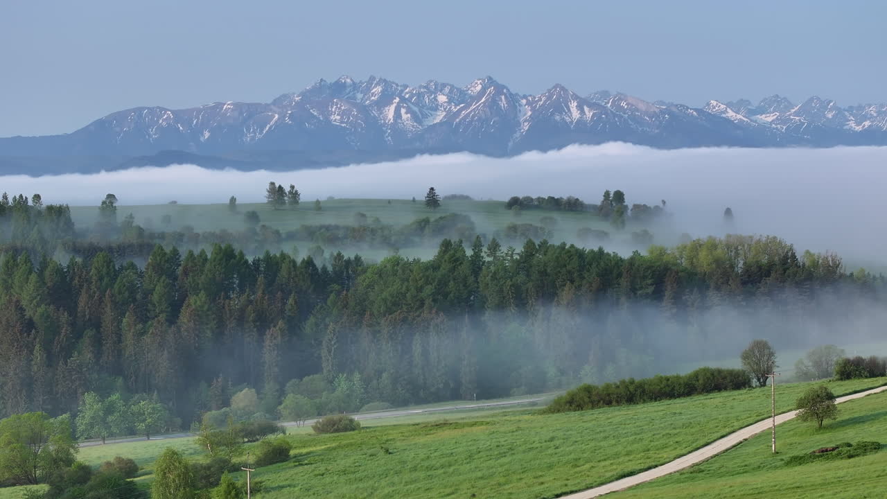 beauty of nature as morning fog and clouds gently blanketing the lush green hills and meadows, creating a serene and cinematic landscape with high mountain range towering in the back.