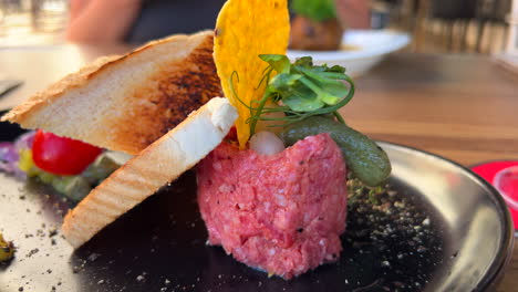 delicious beef steak tartare with toast bread and a pickle on a plate, raw meat dish, 4k shot