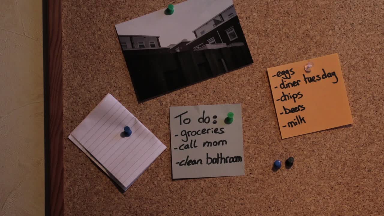 Close Up Shot of a Bulletin Board with a couple of Lists. Groceries is being crossed out!