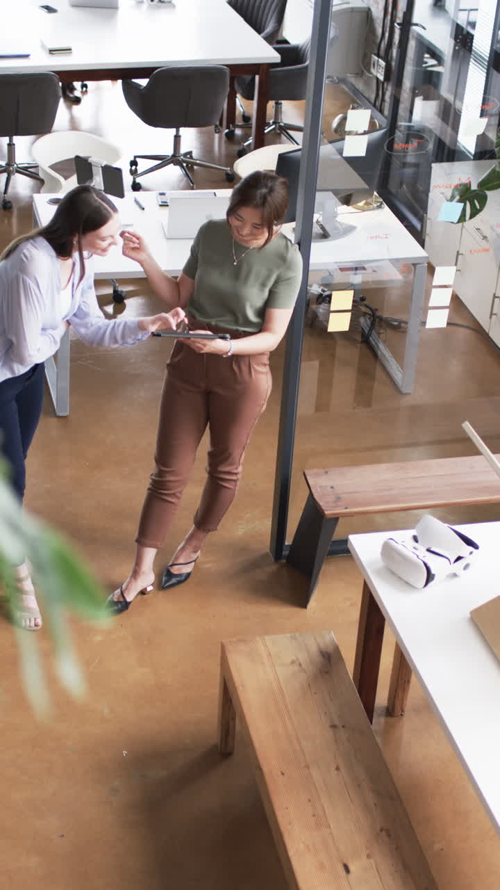 Vertical video: Businesswomen discussing project while looking at tablet in modern office