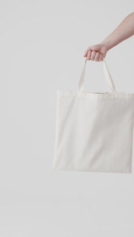 vertical video of hand of caucasian woman with white canvas bag and copy space on white background
