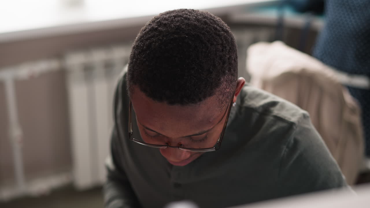 Black man with glasses works at table closeup. Black student studies education sources in library reading hall. African American guy in coworking premise